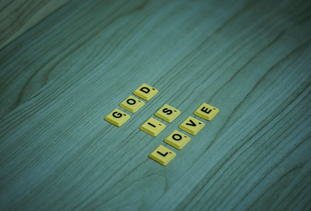 Scrabble tiles on a table that use one row per word to spell out God Is Love.